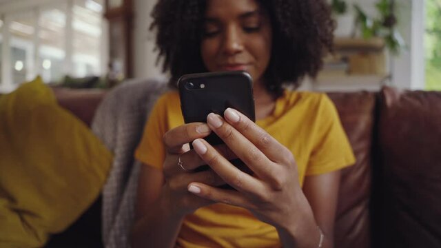 Shot of young woman sitting on sofa holding mobile in her hand checking messages