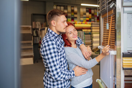Rolette. Couple choosing textile at home decoration store, shop. Making of home interior design during quarantine. Happy man and woman, young family look dreamful, cheerful choosing materials.