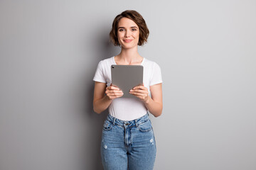 Photo of young attractive positive cheerful woman hold modern gadget tablet isolated over grey...