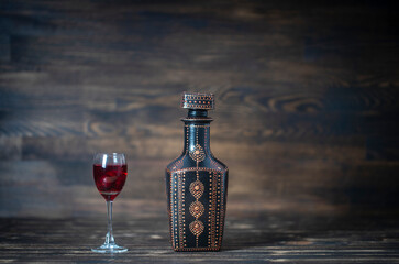 Homemade tincture of red cherry in a decorative bottles and a wineglass on wooden background,...