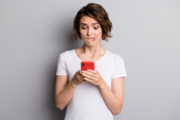 Photo of young woman hold cellphone worried afraid mistake failure bite lips isolated over grey...