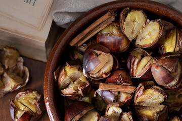 Baked chestnuts with cinnamon in a terracotta bowl. On the side an old book. Autum and winter cozy atmosphere.