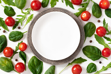 Fresh arugula and spinach leaves lie around a white empty plate top view. Flat lay. Healthy diet food background. Salad ingredients