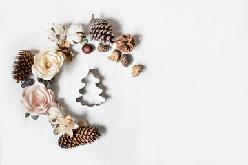 Creative flat lay. Christmas tree gingerbread form and natural elements: origami roses, pebbles, cotton flowers, cones and hazelnuts on white. Minimal top view mock up. Blog mood image, holiday card.