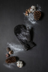 Creative flat lay. Vintage glove with cones, cotton flowers and raw hazelnuts. Winter concept mock up on black background sprinkled with fresh snow. Christmas card or blog. Top view, copy space.