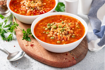 Vegetarian soup with vegetables, green peas, couscous (ptitim paste) and lentils in a white bowl close-up. Maghreb soup berkoukes. North African cuisine.