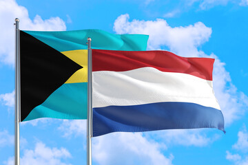 Netherlands and Bahamas national flag waving in the windy deep blue sky. Diplomacy and international relations concept.
