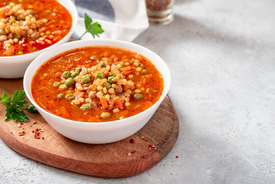 Vegetarian soup with vegetables, green peas, couscous (ptitim paste) and lentils on a grey table. Copy space for text. Maghreb soup berkoukes. North African cuisine.