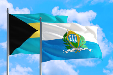 San Marino and Bahamas national flag waving in the windy deep blue sky. Diplomacy and international relations concept.