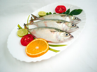 Fresh Indian Mackerel Fish Decorated with herbs and Vegetables on a white plate.