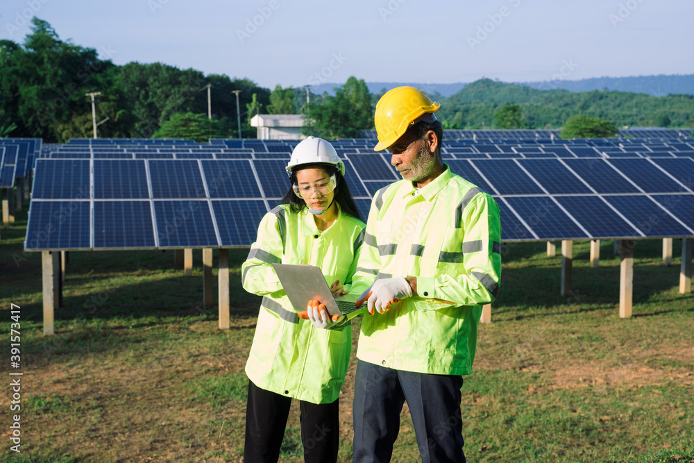 Poster two electrician workers in reflective vests and hard hats working at solar panels and talking about 