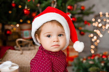 Cute baby Santa sits at home near the Christmas tree with gifts