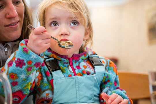 Cute blonde girl eating beef noodle soup in a restaurant with her mother.