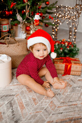 Cute baby Santa sits at home near the Christmas tree with gifts