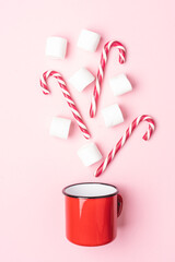 Red mug with marshmallows and caramel canes on pastel pink background. Creative Christmas or New year background. Flat lay on plain background