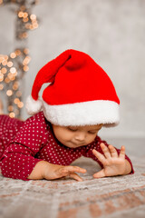 Cute baby Santa sits at home near the Christmas tree with gifts