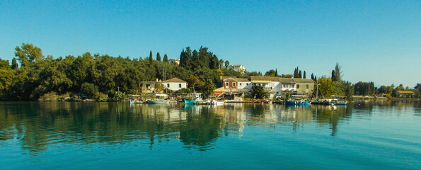 panoramic Greek mediteranean fishing village with cottage houses cypress and olive trees and boats on  calm sea water