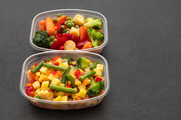 Frozen vegetables in plastic containers on a black background. Copy space. Vegetable salad mix.
