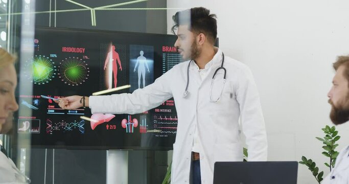 Medical concept where attractive confident experienced bearded medical worker holding a presentation on interactive monitor on risks heart desease theme in front of another colleagues