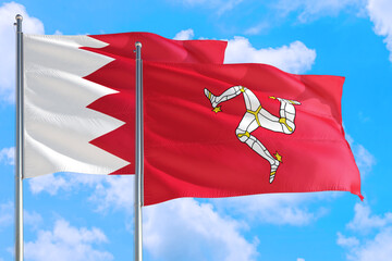 Isle Of Man and Bahrain national flag waving in the windy deep blue sky. Diplomacy and...