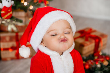 Cute baby Santa sits at home near the Christmas tree with gifts