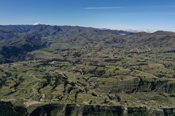 Aerial view of a agricultural area, showing the many grass fields in a hilly area with mountains in the background