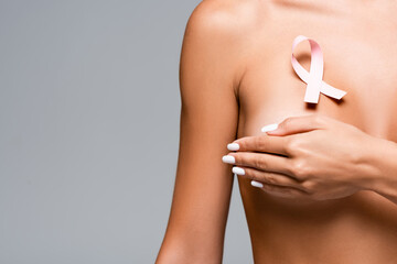 Cropped view of pink ribbon of breast cancer awareness on chest of nude woman isolated on grey