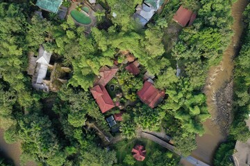 Aerial view of a tropical hotel or lodge located in the jungle and surrounded by lush green foliageand a small brown colored river that is running rapidely