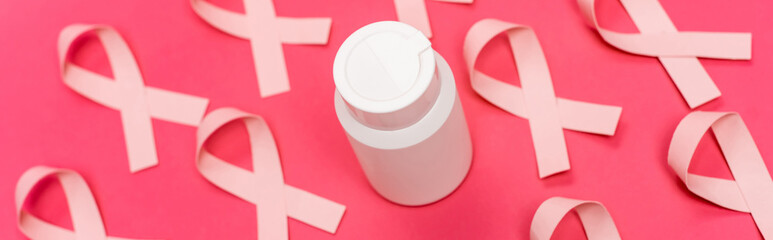 Jar with pills near ribbons of breast cancer awareness blurred on pink background, banner