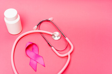 Obraz na płótnie Canvas Stethoscope near pink ribbon of breast cancer awareness and jar with pills on pink background