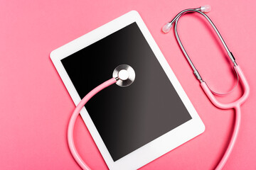 Top view of stethoscope on digital tablet with blank screen on pink background
