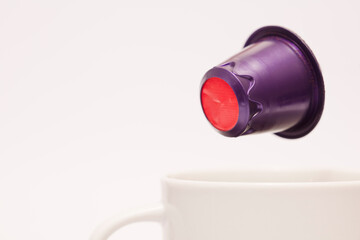 purple and red capsule, flying over white porcelain cup, coffee powder and white background