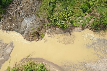 Aerial view of a landslide covered in the dry tree trunks alonside a tropical river