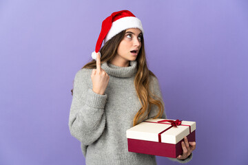 Girl with christmas hat holding a present isolated on white background thinking an idea pointing the finger up