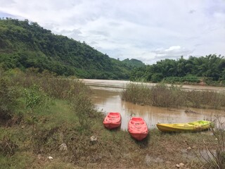 Three canoes without people put on the riverbank of a large brown river in Thailand