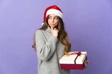 Girl with christmas hat holding a present isolated on white background having doubts and thinking