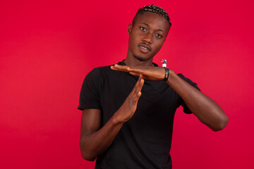 Young African American handsome man standing against red background feels tired and bored, making a timeout gesture, needs to stop because of work stress, time concept.