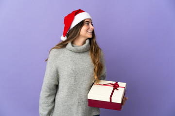 Girl with christmas hat holding a present isolated on white background looking to the side and smiling