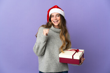Girl with christmas hat holding a present isolated on white background celebrating a victory in winner position