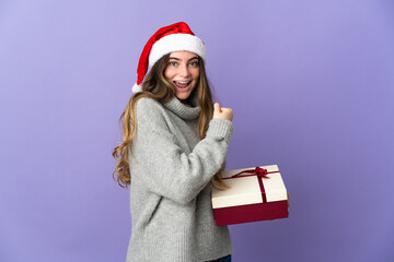 Girl with christmas hat holding a present isolated on white background celebrating a victory