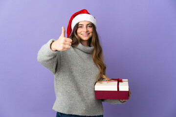 Girl with christmas hat holding a present isolated on white background with thumbs up because something good has happened