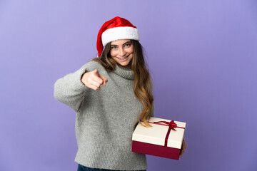 Girl with christmas hat holding a present isolated on white background pointing front with happy expression