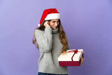 Girl with christmas hat holding a present isolated on white background frustrated and covering ears