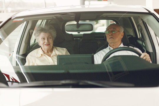 Old couple in a car salon. Family buying the car. Elegant woman with her husband. Senior by a car.