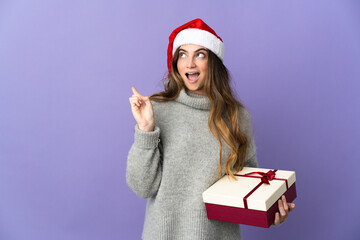 Girl with christmas hat holding a present isolated on white background intending to realizes the solution while lifting a finger up
