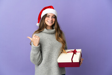 Girl with christmas hat holding a present isolated on white background pointing to the side to present a product