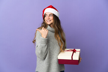 Girl with christmas hat holding a present isolated on white background pointing to the side to present a product