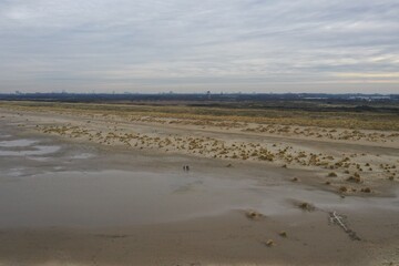 Aerial view over a beach with three people walking over the sand and the low dunes in the background