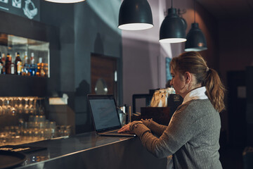 Woman working remotely on her laptop computer managing her work sitting at the table in a cafe. Female hands typing on laptop keyboard