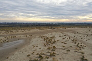 Aerial view of a broad sand beach and the low dunes in Europe with a city in the background and a colored cloudscape at sunset